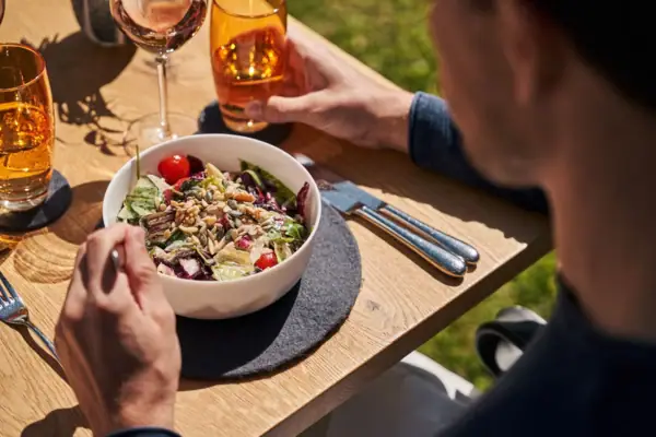 Man eats salad and drinks wine at the table.