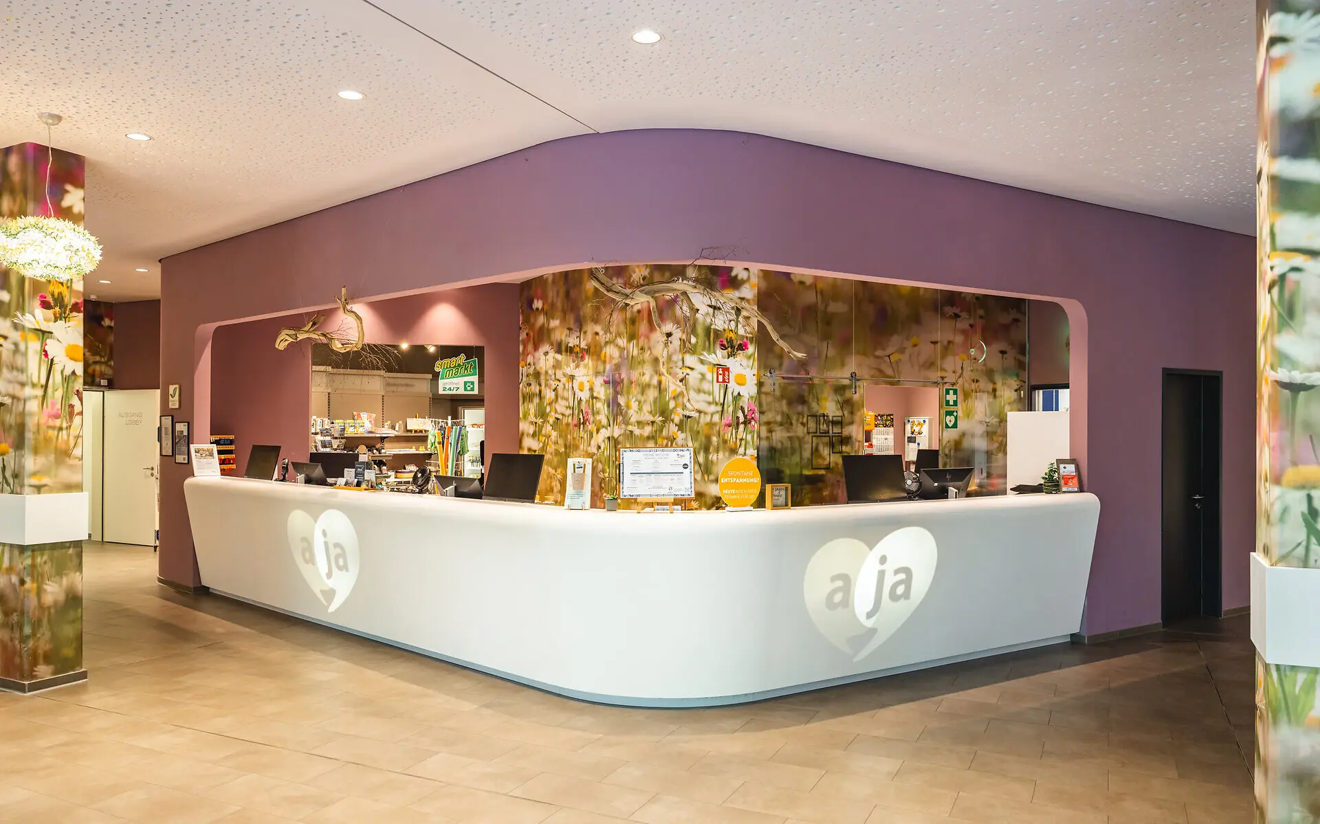 The reception with natural, realistic flower wallpaper and purple colors. The desk is white and has aja in a heart written on each side. The lighting is warm. 