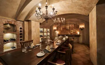 A long dining table set with plates and glasses under a chandelier in an indoor setting.
