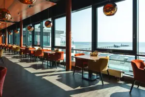 A room with tables and chairs and a window overlooking the ocean.