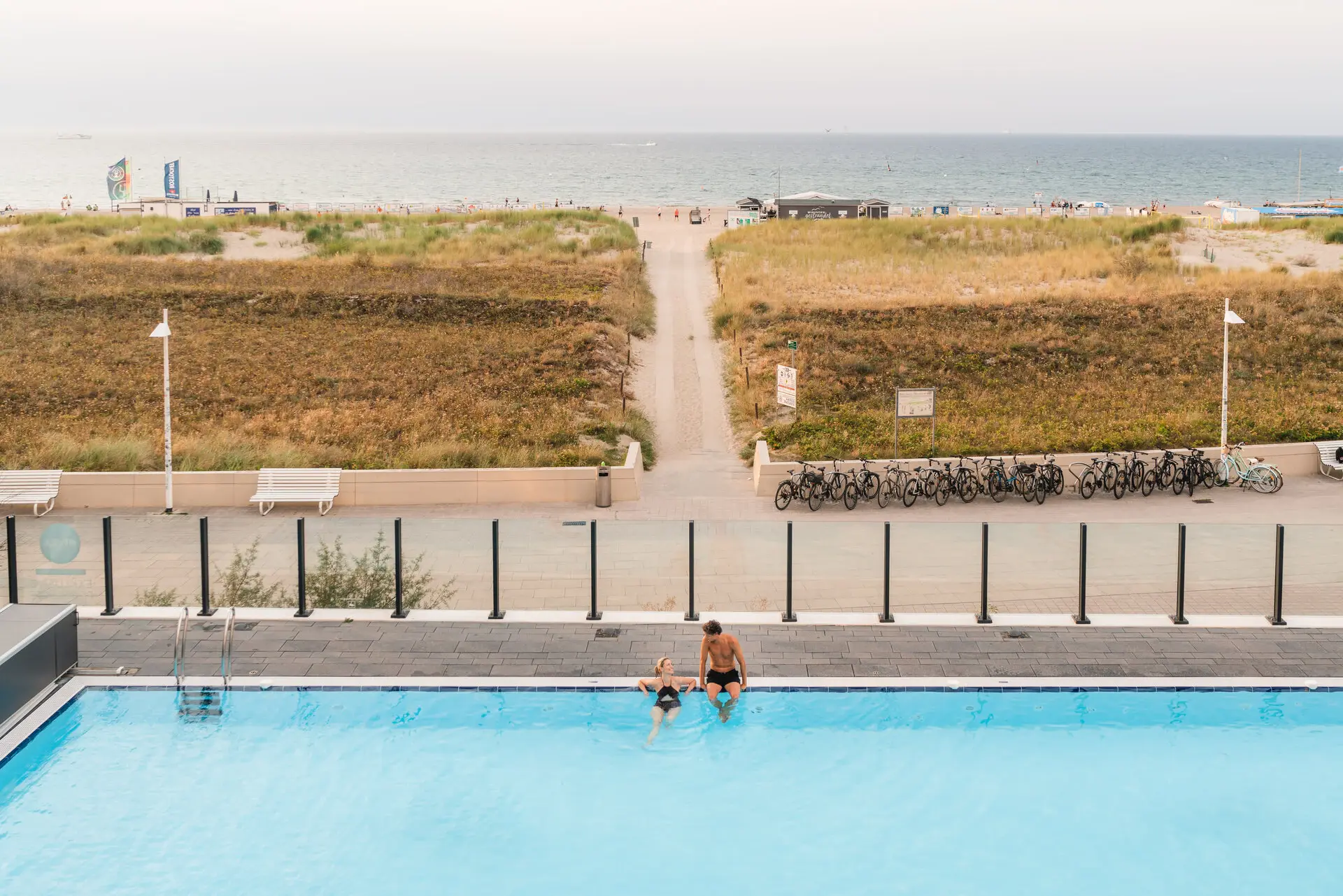 A man and a child in the pool with a beach and bicycles in the background.