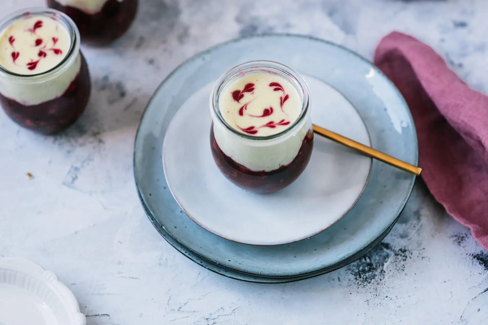 A glass with red liquid and a spoon on a plate.