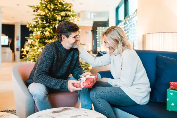 Christmas A man and a woman are sitting on a sofa with a present.
