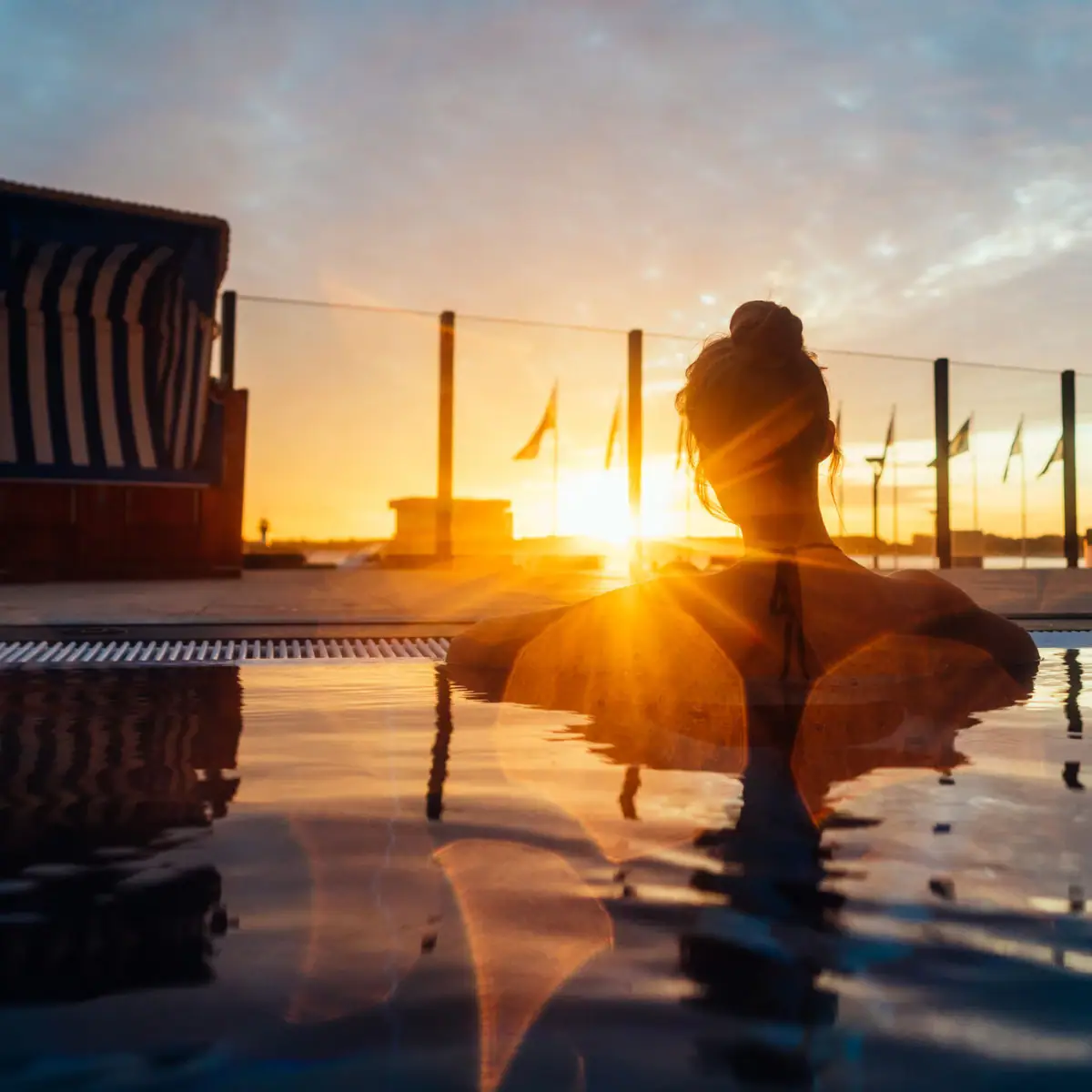 A woman relaxes in a pool with the sunset in the background.