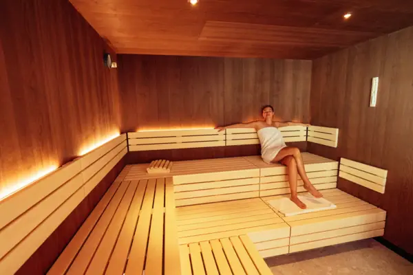 A woman wrapped in a towel is sitting on a bench in a sauna.