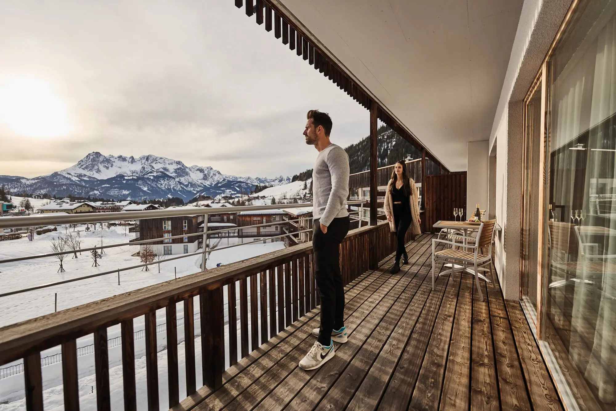A man and a woman stand on a terrace and look out over snow-covered mountains.