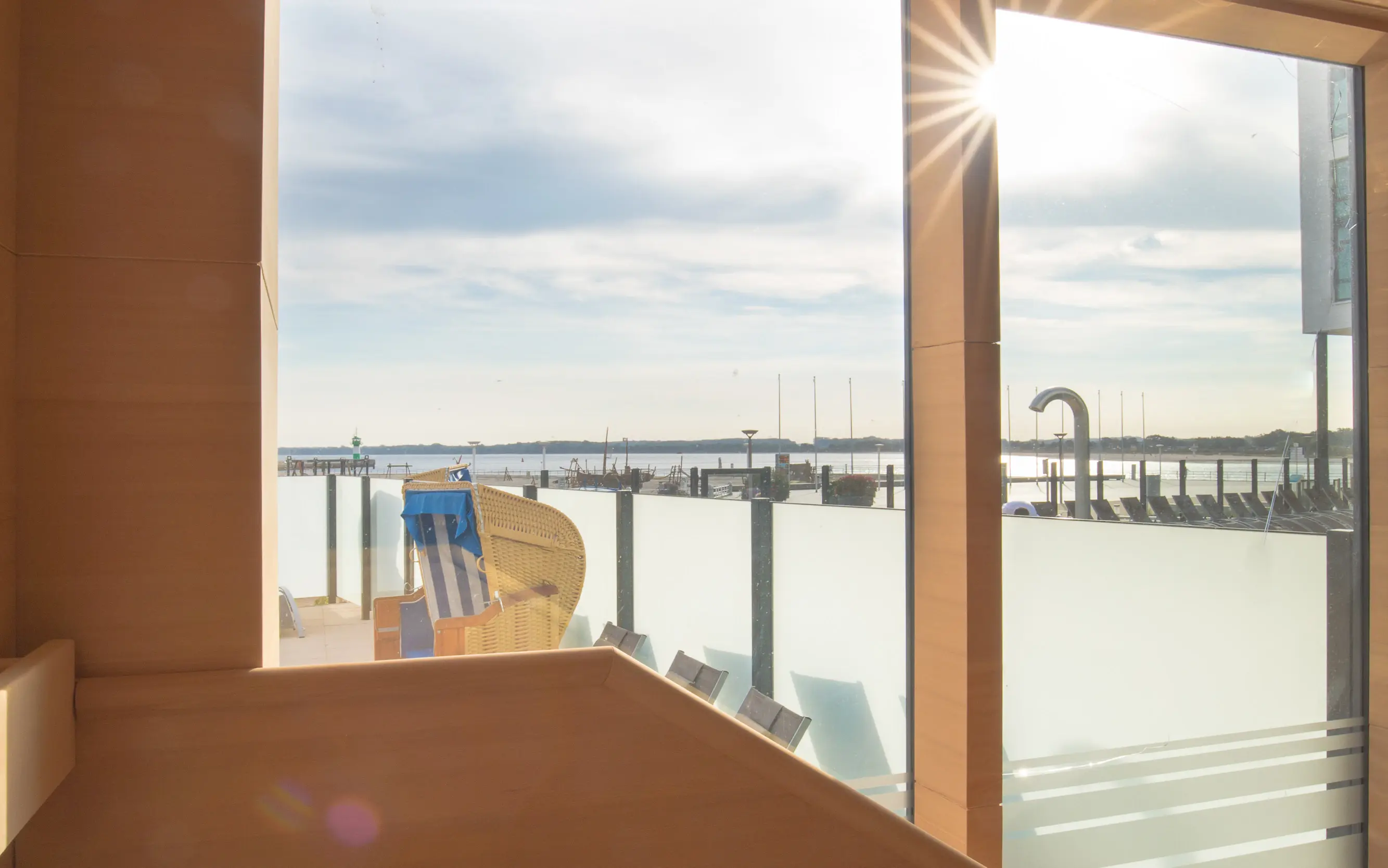 A serene sauna interior with wooden benches, offering a stunning view of the marina and the glistening water through large glass panels as sunlight streams in.