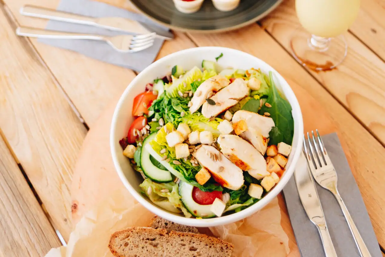 Salad with chicken A plate of food and a drink on a table.