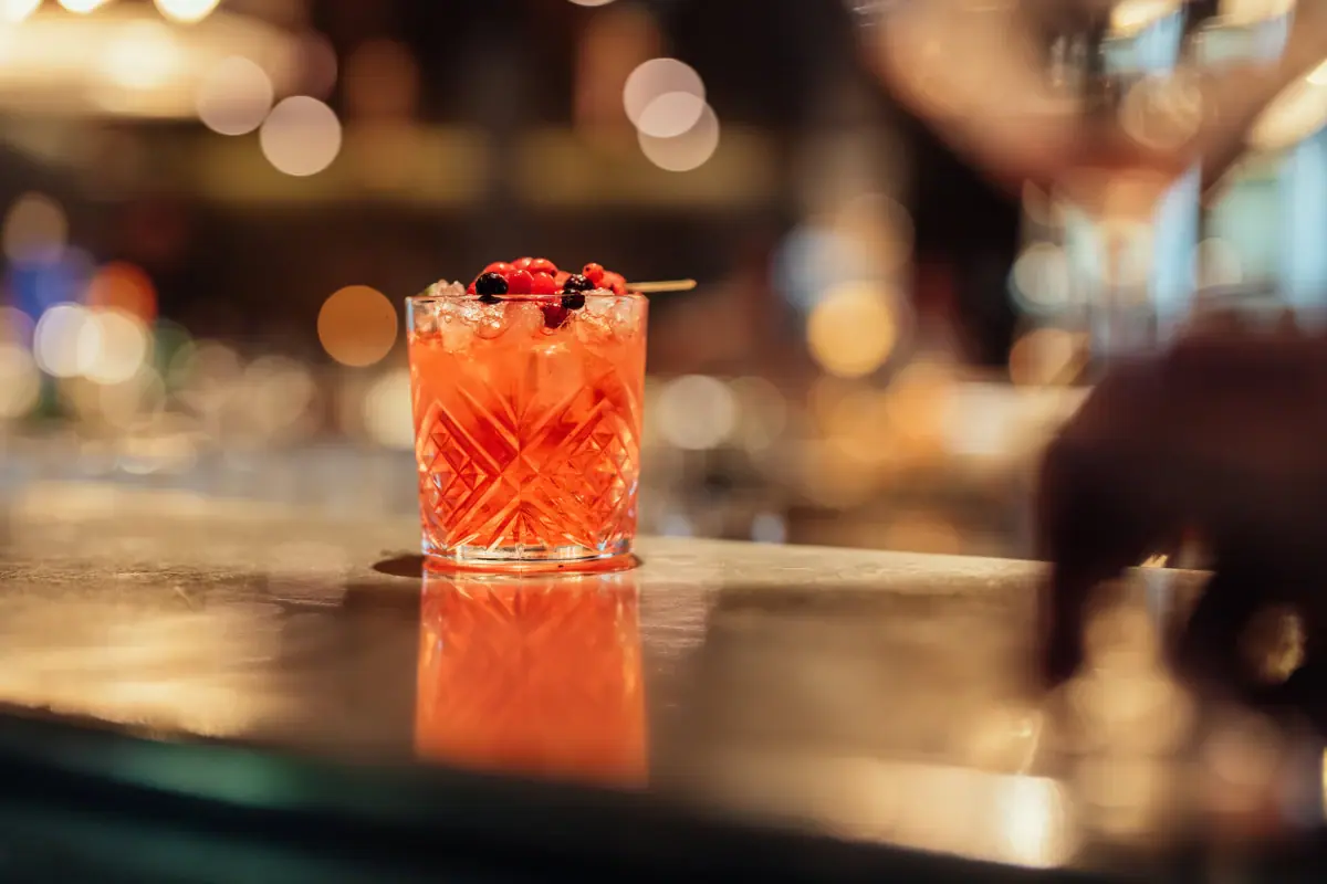 A glass containing a cocktail, garnished with berries.
