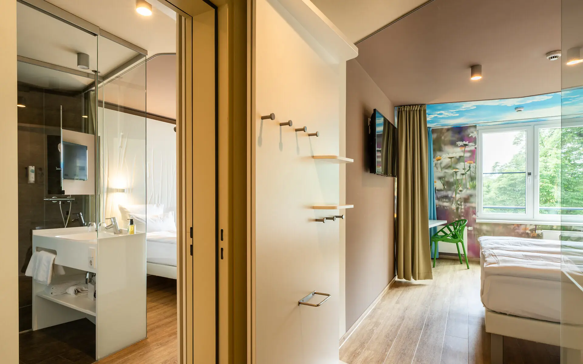 Two hotel rooms connected through a connecting door, each with comfortable beds facing each other, coat hangers and a glas bathroom in the left. 