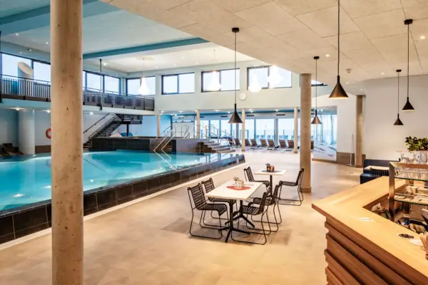 An indoor swimming pool in a building with a ceiling and furniture.