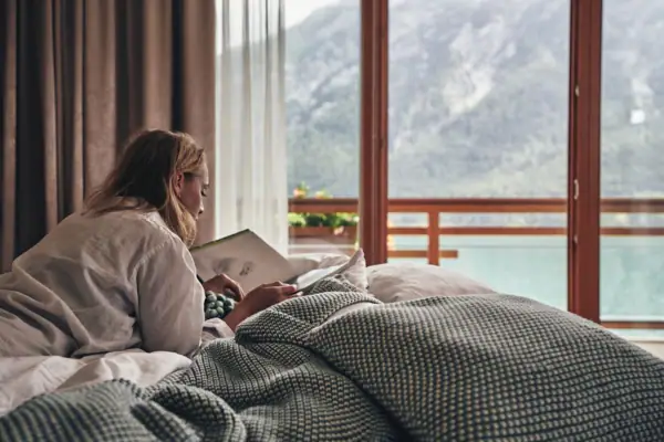 A woman lies on a bed and reads a book.