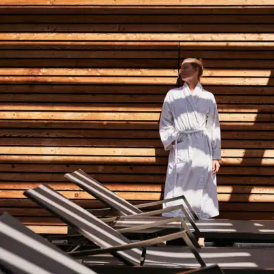 A woman in a white bathrobe stands in front of a wooden wall.