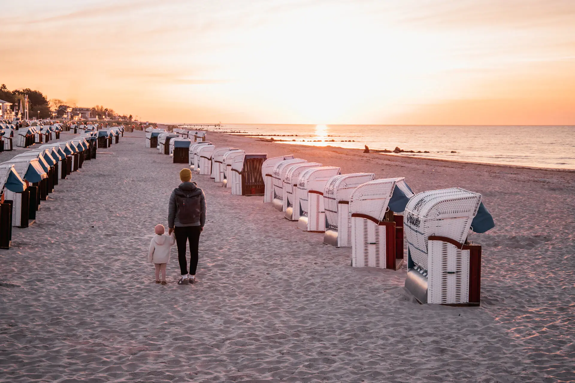 A woman and a child walk along the beach, wiping the lined up beach chairs