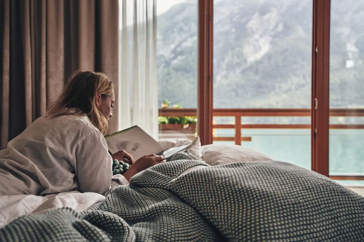 Room with a view of Lake Achensee Woman lying on a bed and reading a book.
