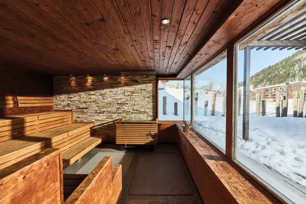 Sauna benches with a sauna heater and a stone wall. Also a large window.