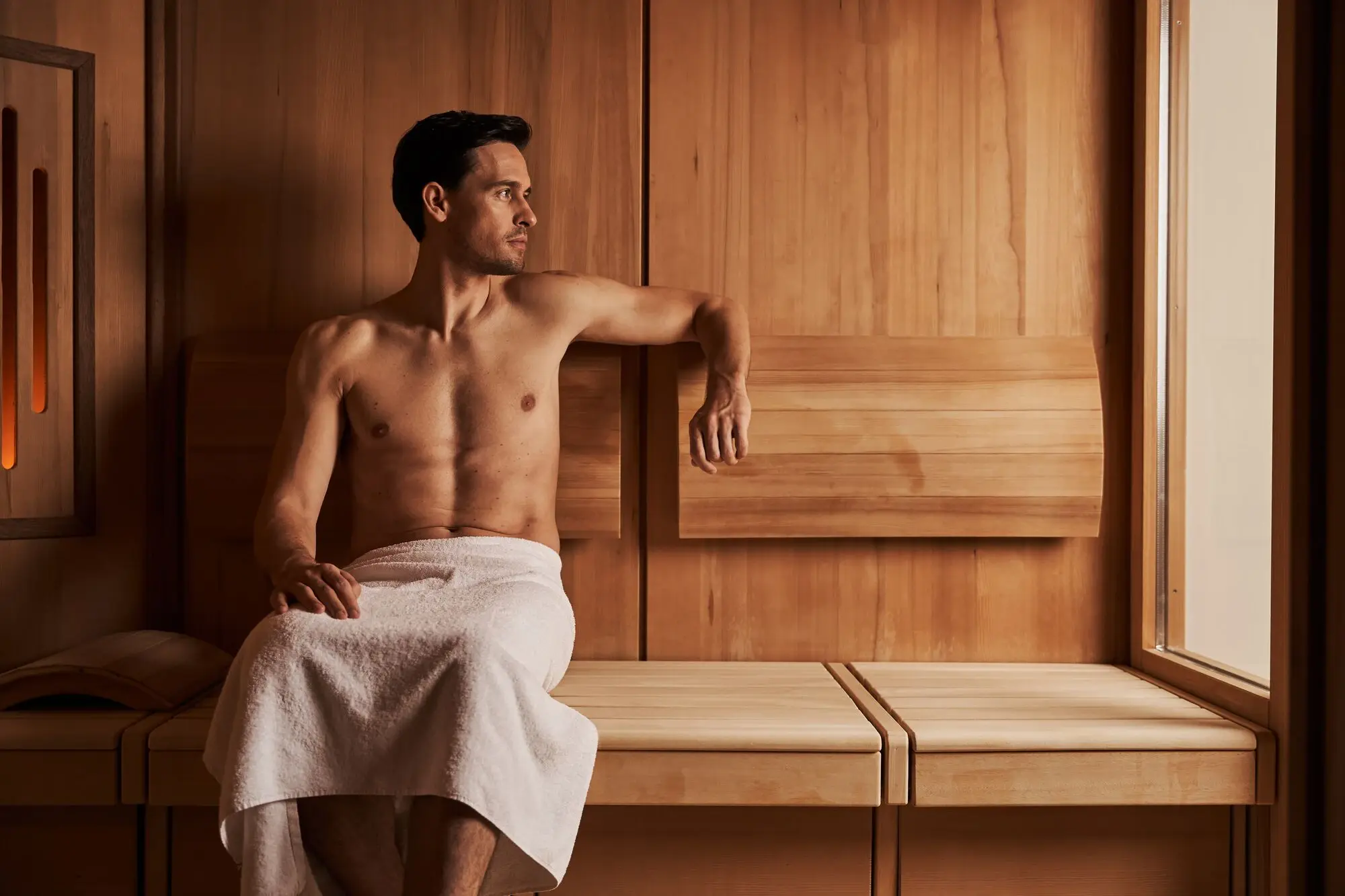 Man sitting in a sauna, wearing a towel.