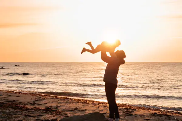 A woman is holding a baby on the beach.