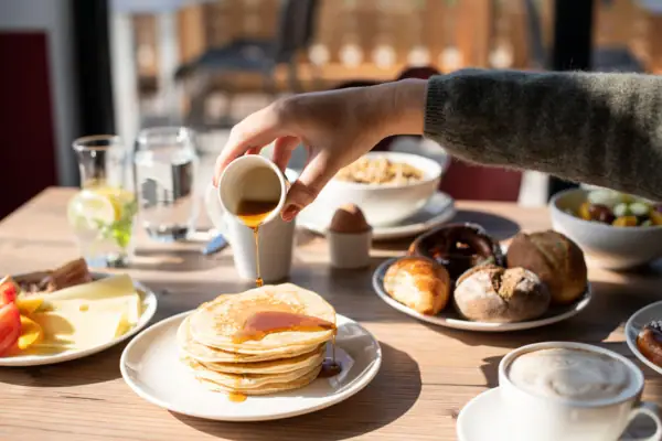 One person pours syrup onto a stack of pancakes.