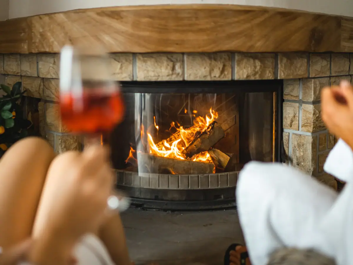 Sauna bar at aja Warnemünde A person holds a glass of wine in front of a fireplace.