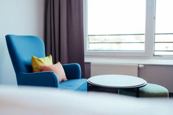 Blue armchair with cushions and a round table in front of a window.
