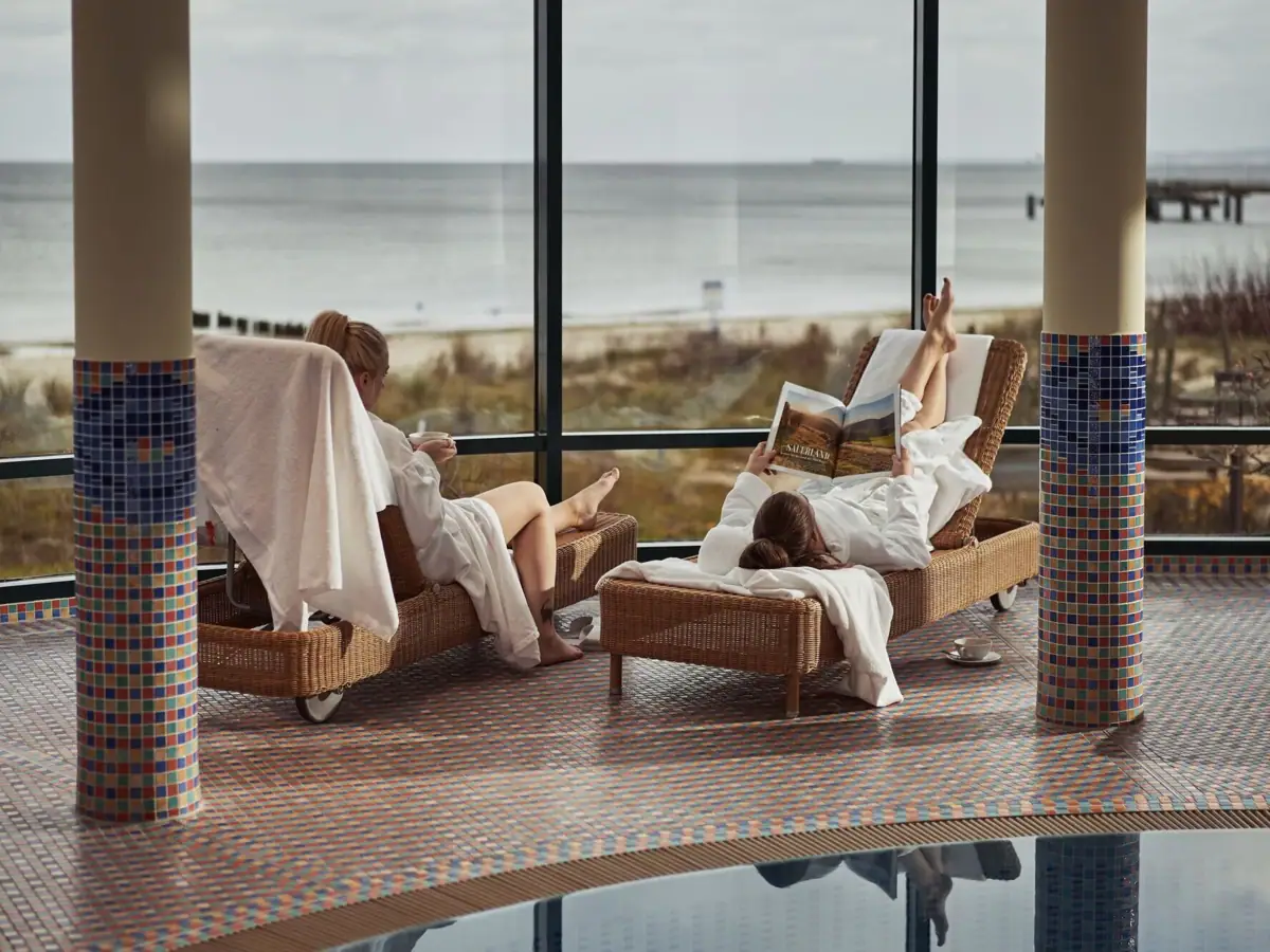 A group of women in white robes lie on chairs by the pool.