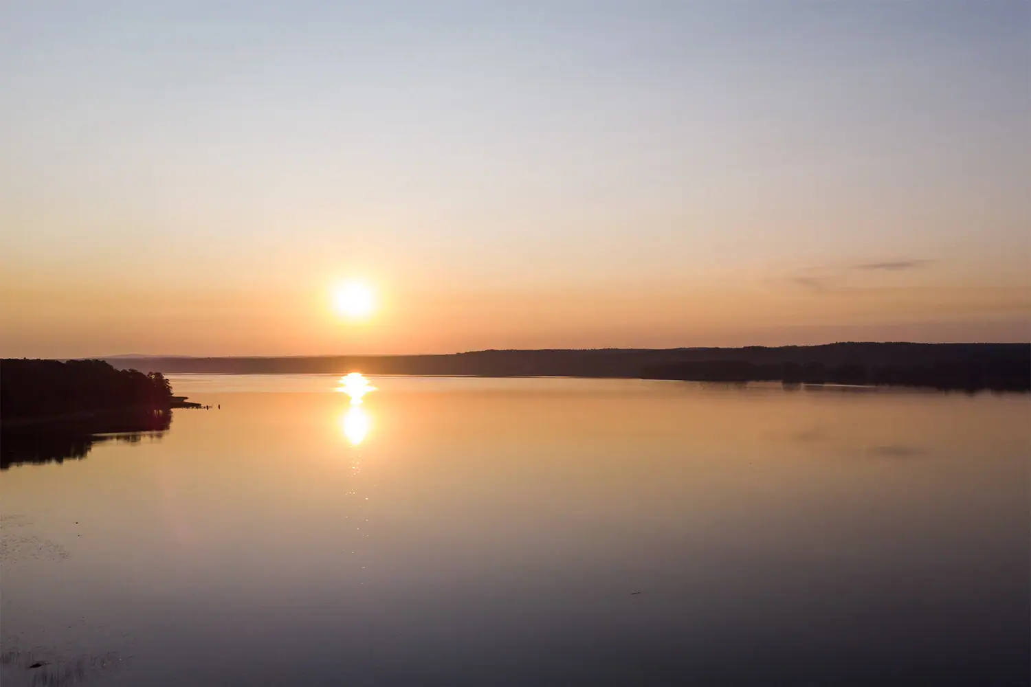 Sunset over a lake with calm water and a colourful sky.