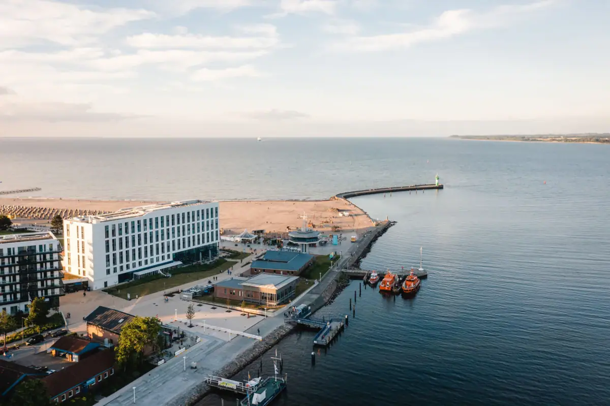 The aja Travemünde, situated right on the waterfront, with boats and buildings in the background.