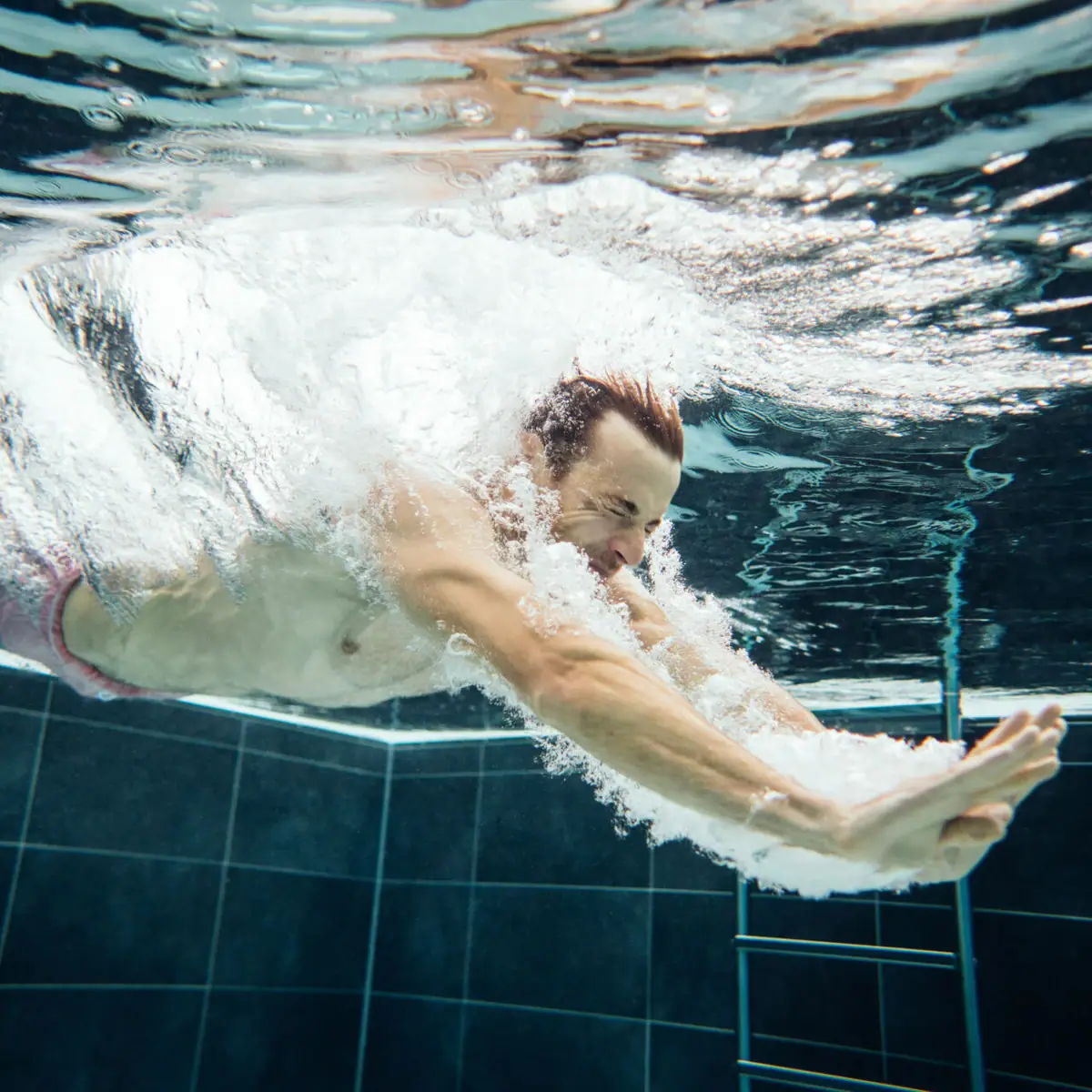 Dive into the pool A man swims under water with air bubbles.