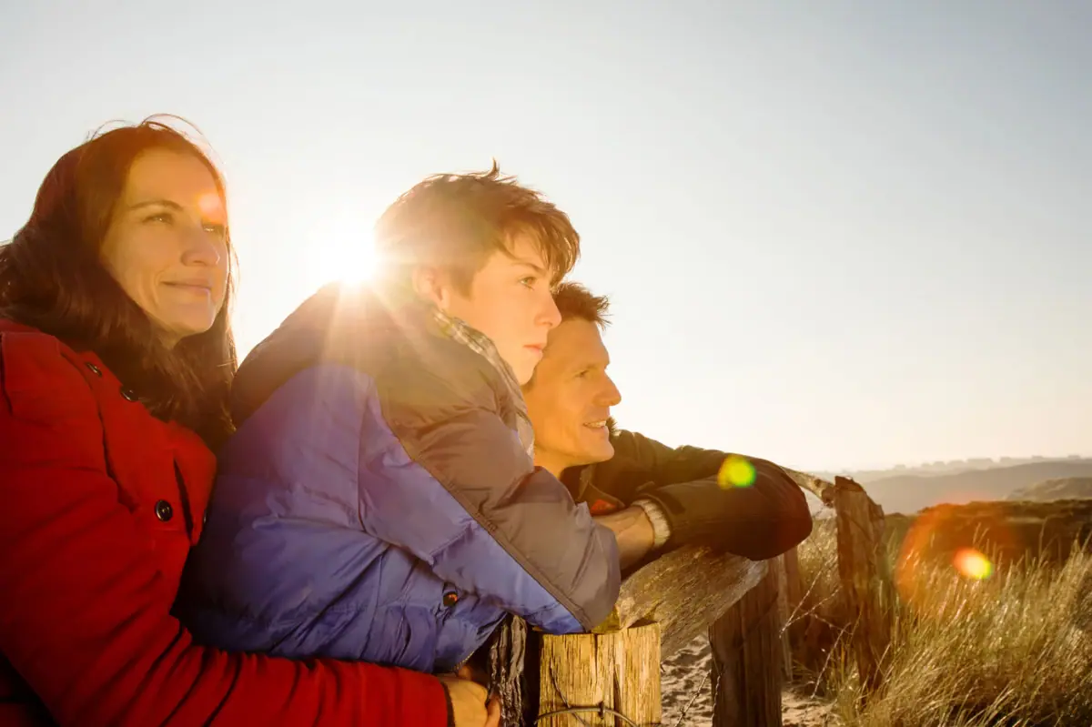 A group of people lean against a fence outside.