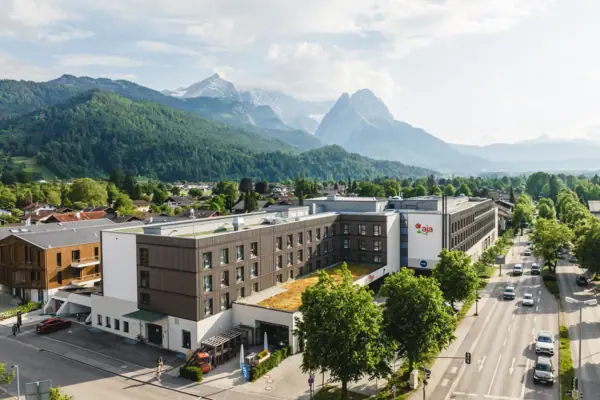 aja Hotel Garmisch-Partenkirchen A building with trees and mountains in the background.