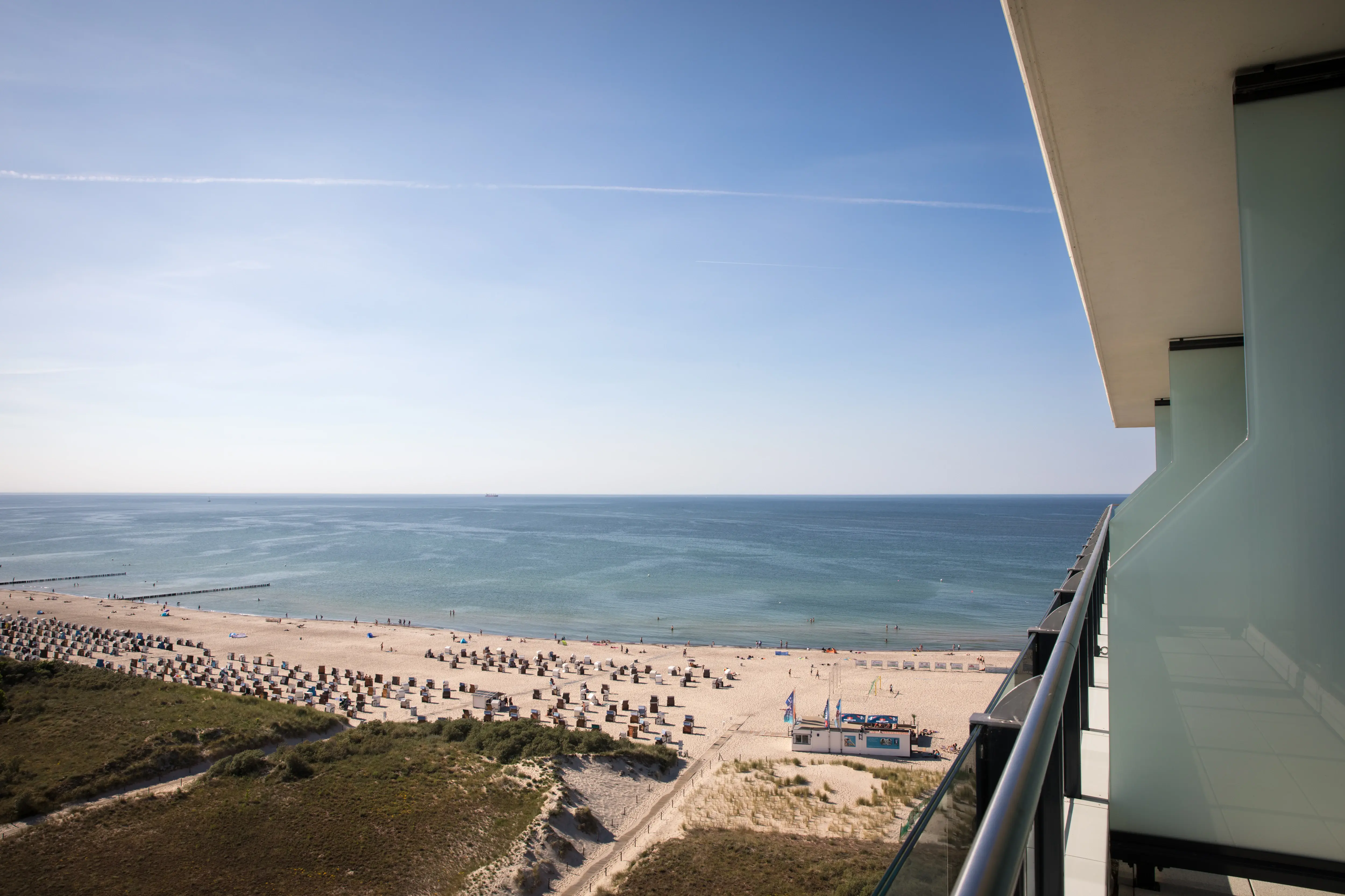 View from a hotel balcony overlooking a sandy beach with rows of beach chairs, a calm blue sea, and a clear sky, offering a peaceful and picturesque coastal scene.