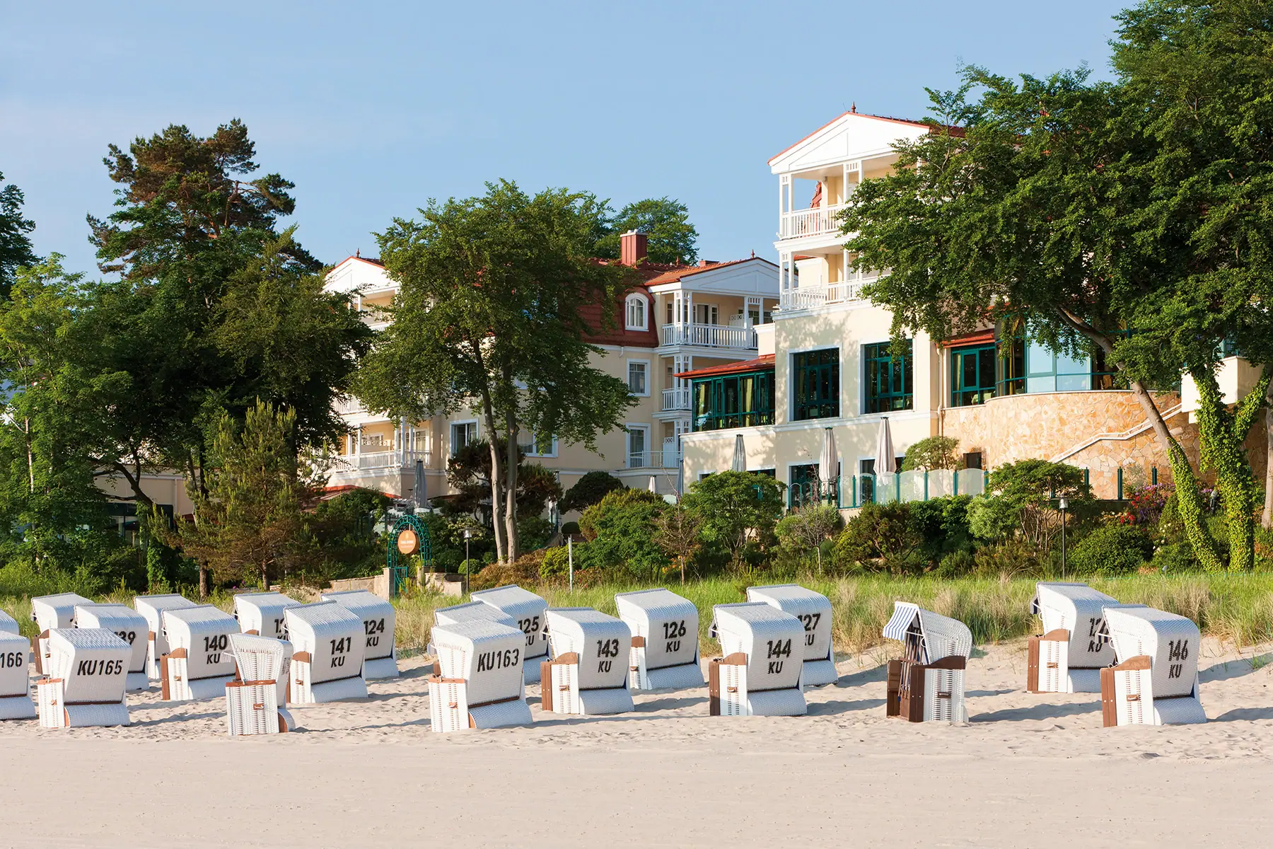 A group of beach chairs on the beach with the aja Strandhotel Bansin in the background.
