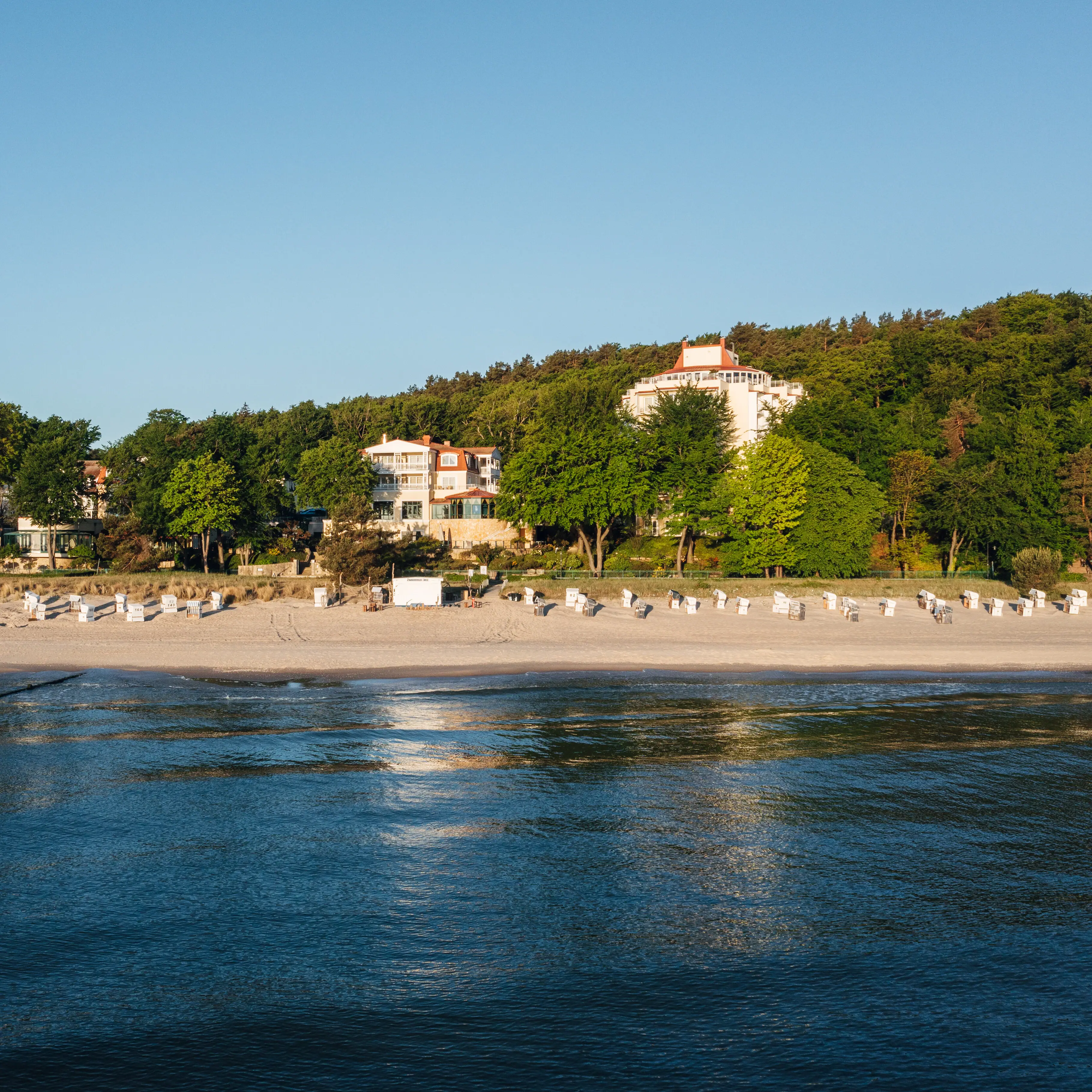 Beach with white buildings and trees in the foreground.