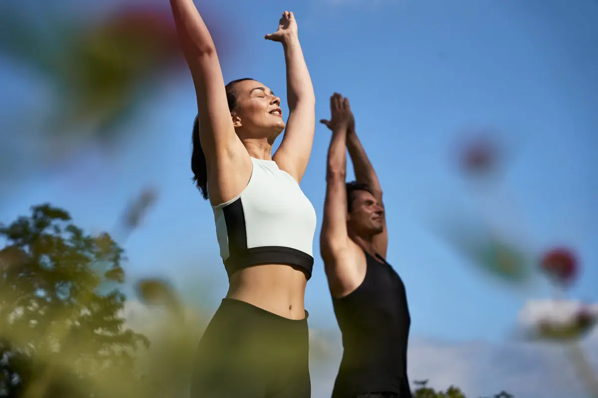 A man and a woman outdoors, with their arms raised.