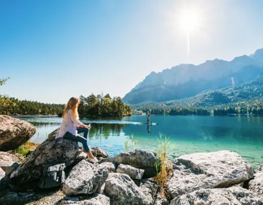 A woman sitting on a rock by a lake with mountains in the background.
