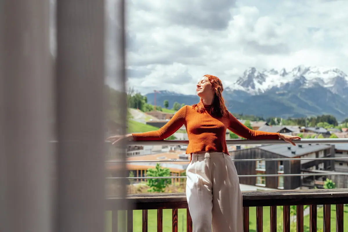 A woman is standing on a balcony with her arms outstretched.