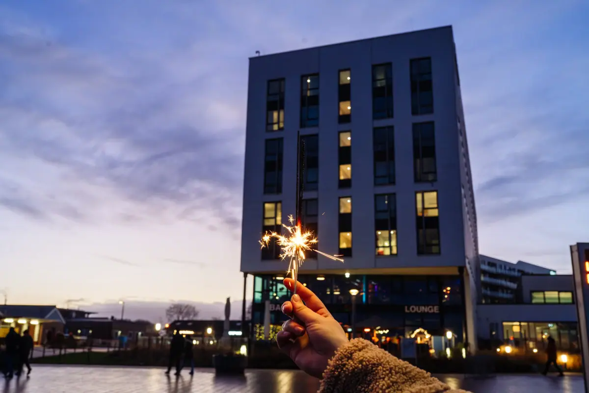 A hand is holding a sparkler in front of a building.