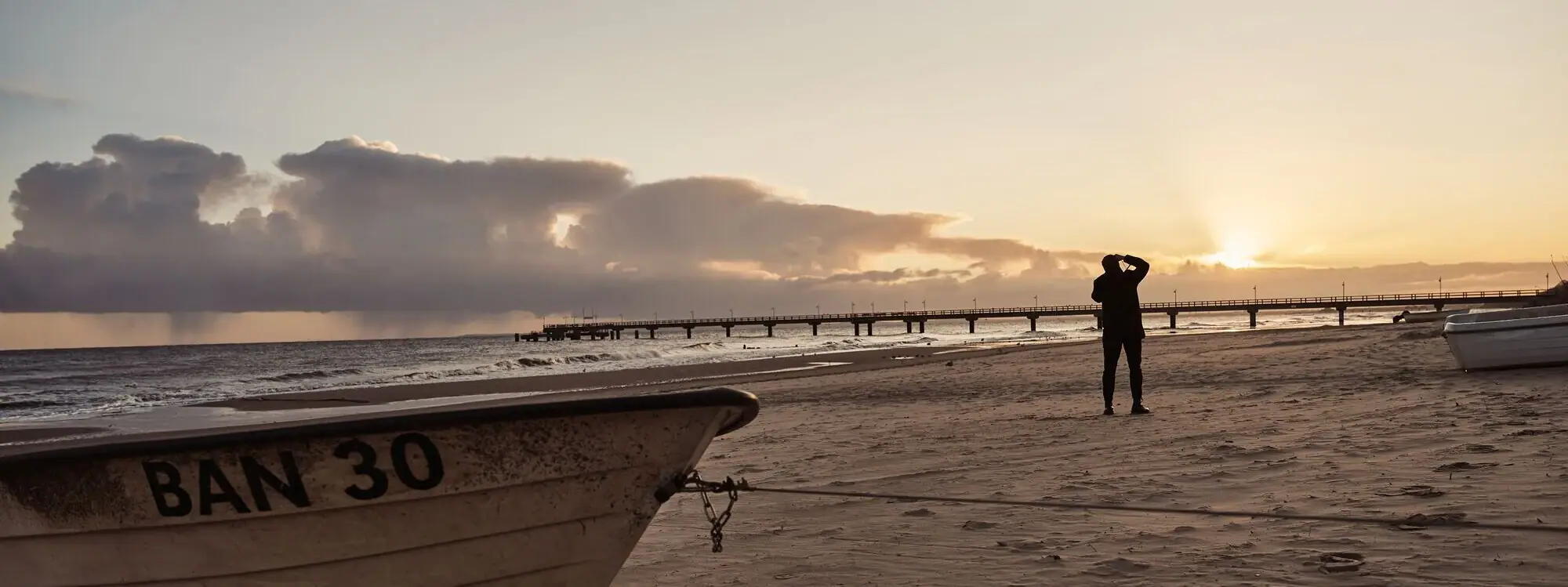 A person standing on a beach with a boat on the shore.
