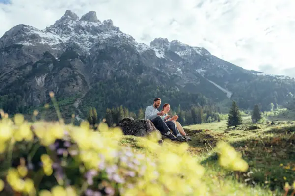 A man and a woman are sitting on a rock in front of a mountain.
