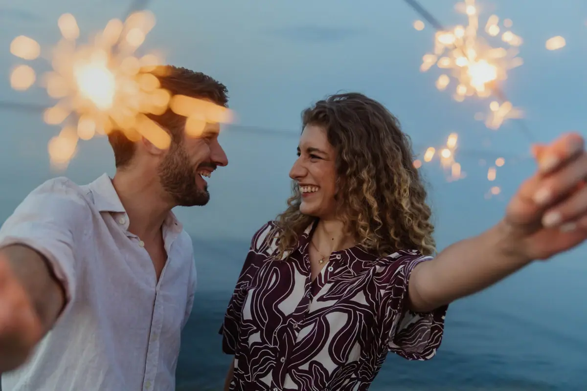 A man and a woman are standing side by side holding sparklers.