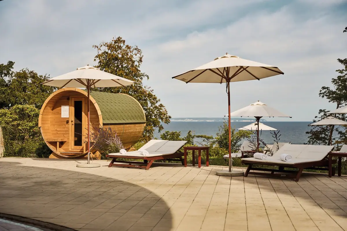 Sun loungers and parasols next to a barrel sauna by the water’s edge