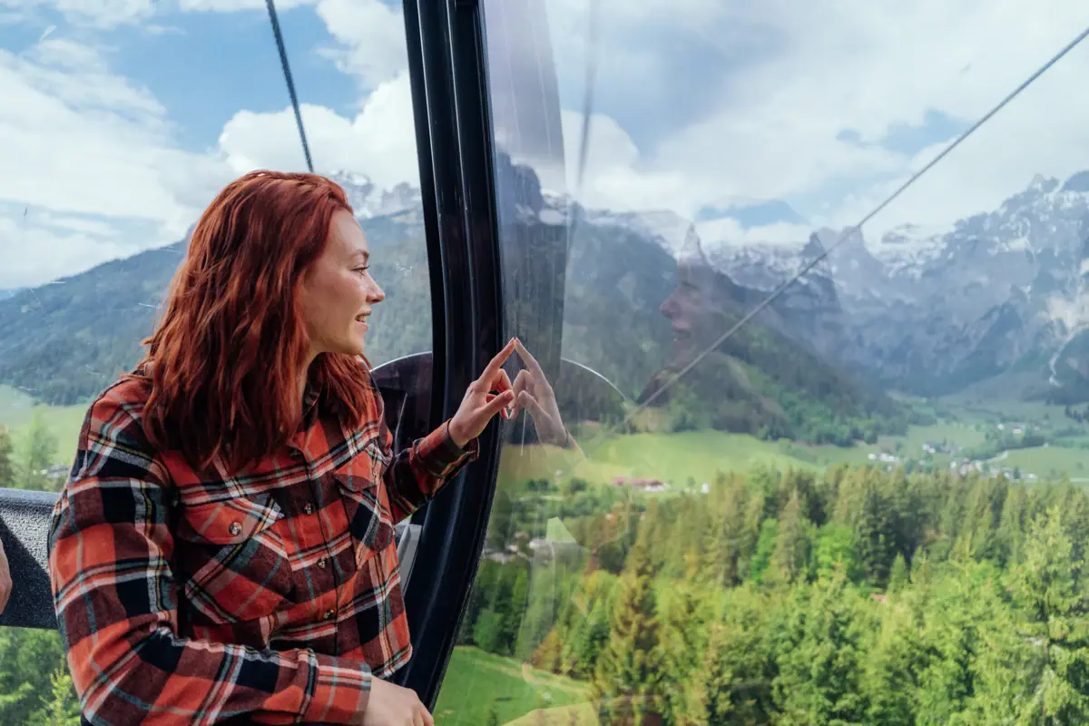 A woman is looking out of a gondola window at the mountains.