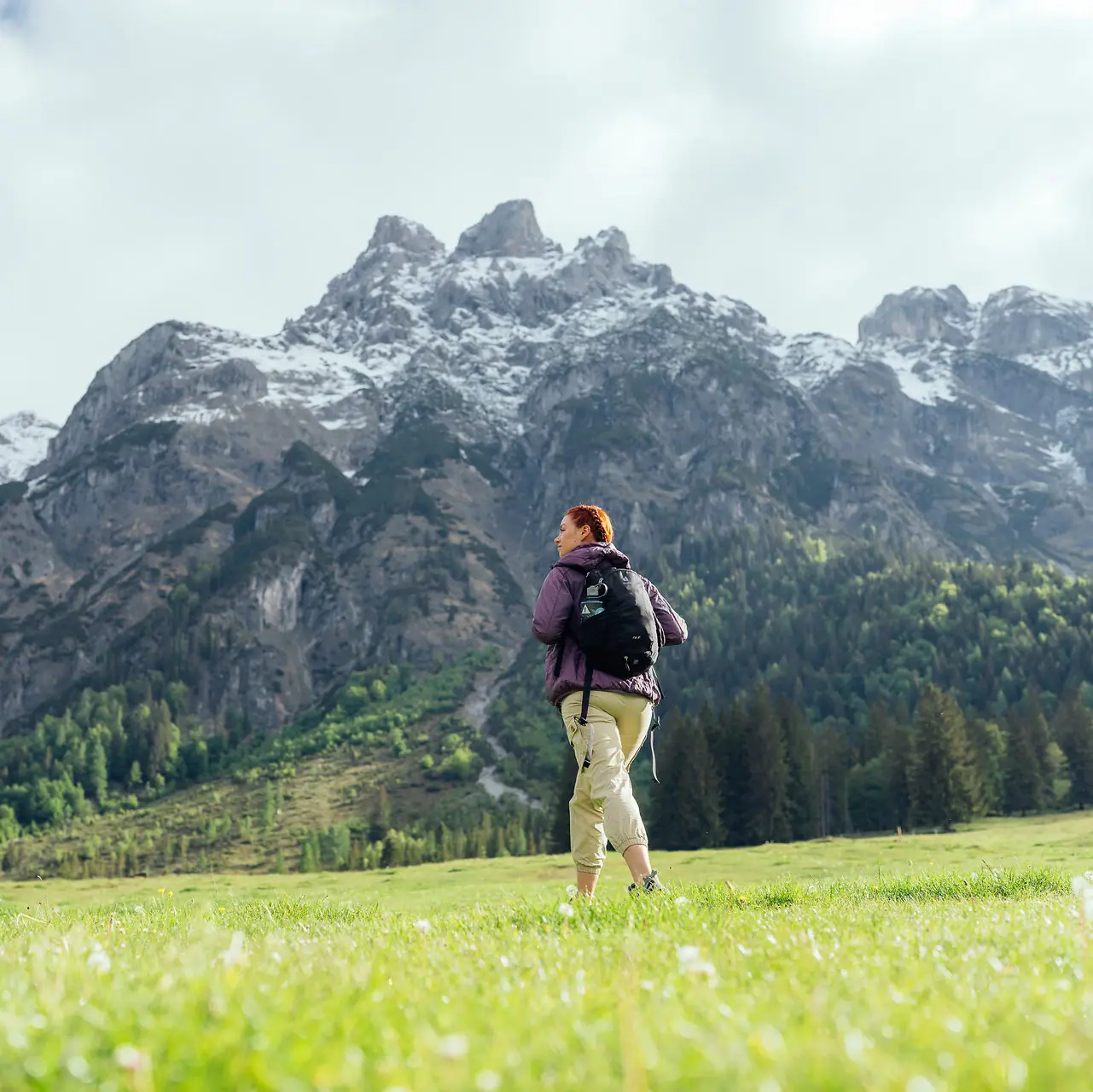 A woman is standing in a field with mountains in the background.