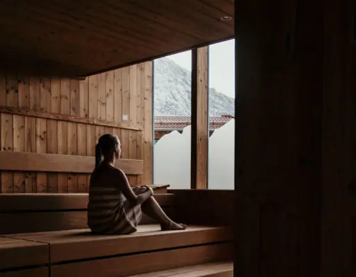 A woman sitting on a wooden bench indoors near a window.