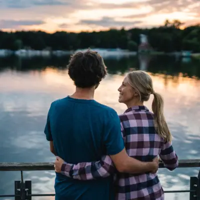 A man and woman hugging by a lake under a cloudy sky.